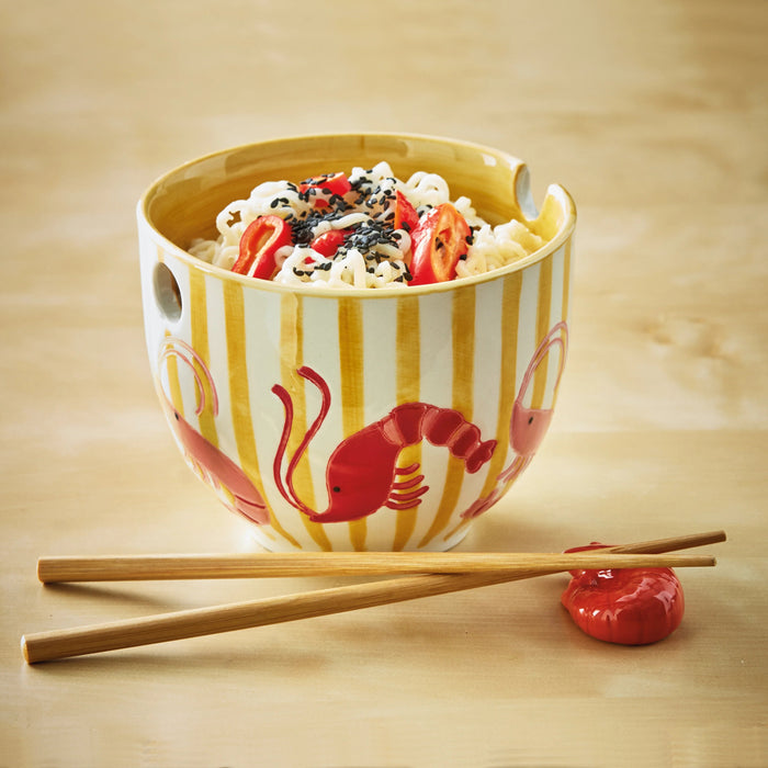 Ceramic bowl with striped design and red lobster illustration, containing a dish with noodles and vegetables on a wooden surface.