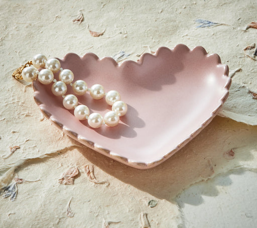 Pink shell-shaped dish with a pearl necklace on a textured beige surface