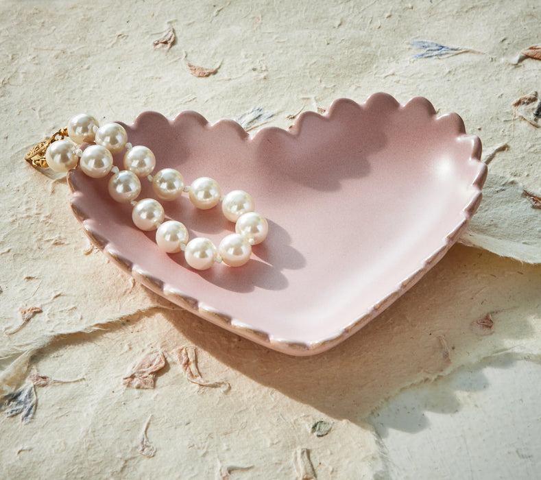 Pink shell-shaped dish with a pearl necklace on a textured beige surface