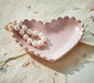 Pink shell-shaped dish with a pearl necklace on a textured beige surface