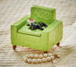 Green textured armchair with a black cat figurine and coffee cup, pearl necklace on beige fabric background