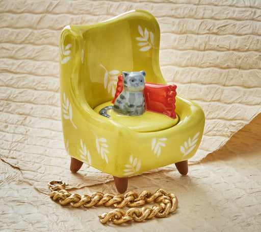 Yellow chair with a small cat figurine and red cushion on a textured beige surface.