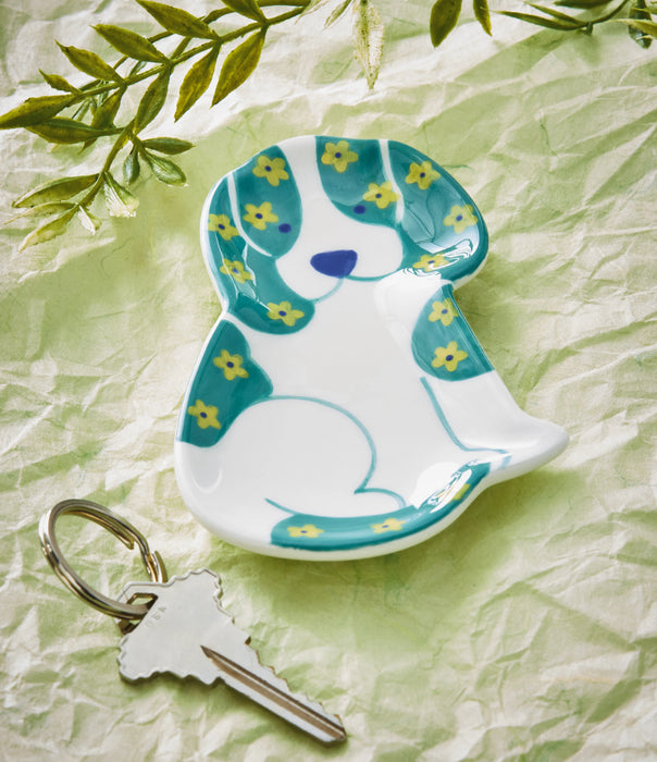 Decorative dog-shaped keychain on a textured green surface with leaves.
