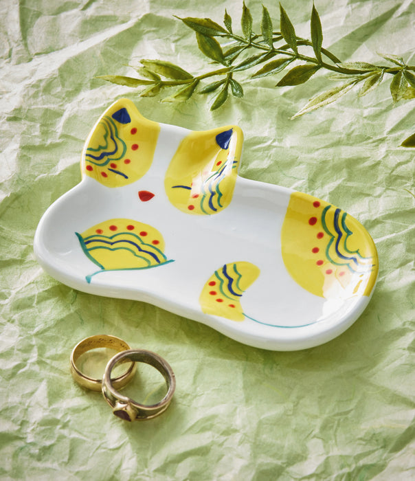 Ceramic cat-shaped trinket dish with decorative patterns on a green crumpled paper background.