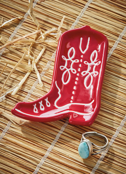 Red ceramic boot with white designs on a woven surface, accompanied by a silver ring with a turquoise stone.