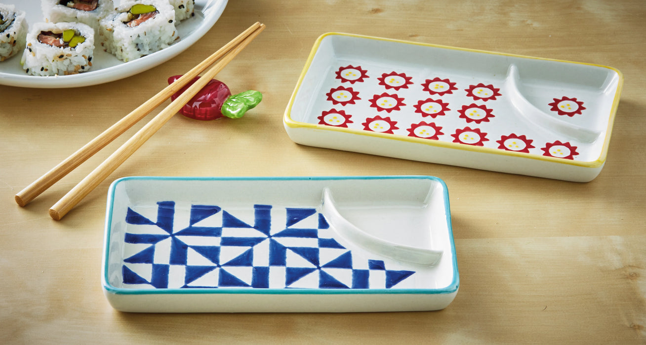 Two ceramic trays with geometric designs on a wooden surface with sushi and chopsticks.
