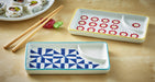 Two ceramic trays with geometric designs on a wooden surface with sushi and chopsticks.
