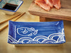 Blue ceramic plate with fish design on a wooden surface with salmon and soy sauce.