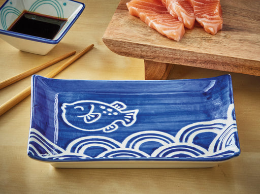 Blue ceramic plate with fish design on a wooden surface with salmon and soy sauce.