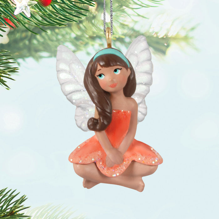 Fairy ornament with white wings and an orange dress on a light blue background