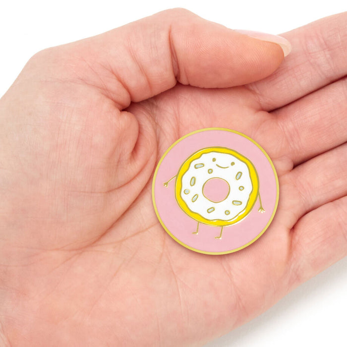 Circular pink badge with a donut design held in a hand against a white background