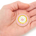 Circular pink badge with a donut design held in a hand against a white background