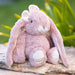 Pink plush bunny sitting on a wooden log with a blurred green background