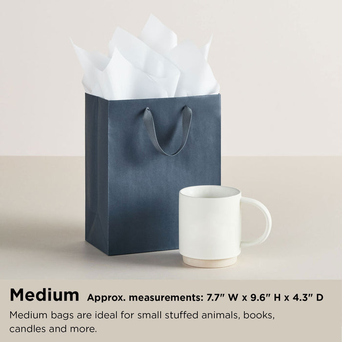 Blue gift bag with white tissue paper and a white mug on a beige background