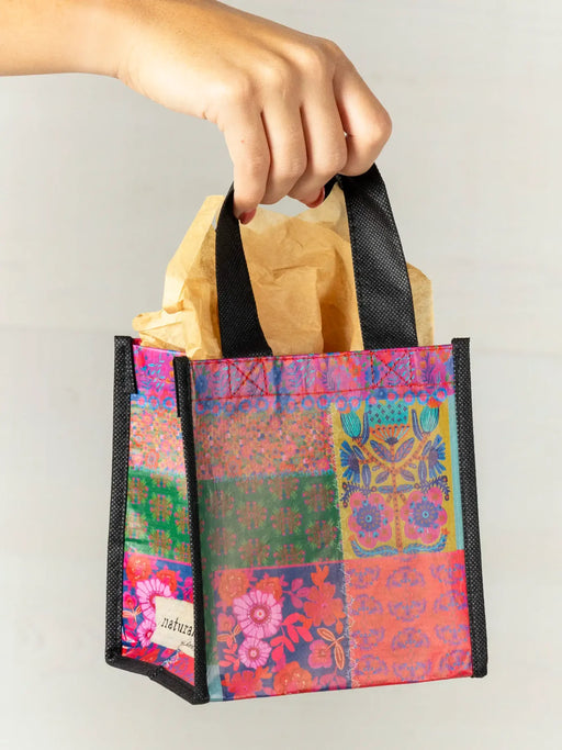 Colorful patchwork bag with black handles holding a brown paper bag against a light gray background