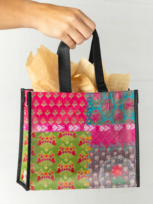 Colorful patterned shopping bag with black handles held by a hand against a light gray background