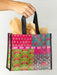 Colorful patterned shopping bag with black handles held by a hand against a light gray background