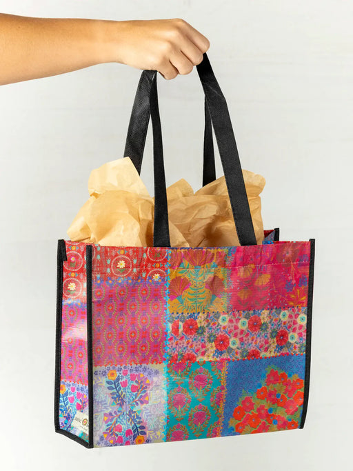 Colorful patchwork tote bag with black handles held by a person against a white background