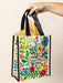 Colorful tote bag with floral design and text held by a hand against a beige background