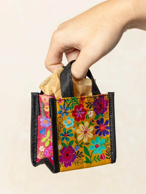 Colorful floral-patterned bag held by a hand against a beige background