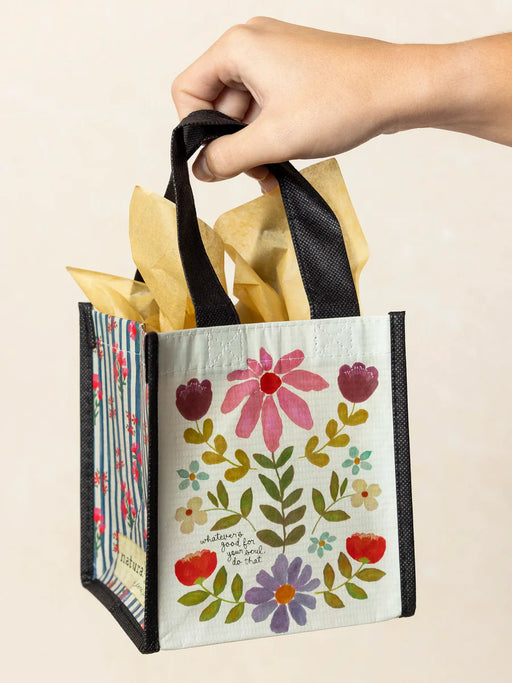 Hand holding a floral gift bag with black handles against a beige background