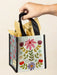Hand holding a floral gift bag with black handles against a beige background