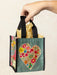 Hand holding a small gift bag with a floral heart design on a beige background