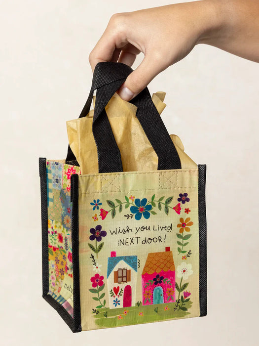 Hand holding a small decorative bag with floral designs and house illustration on a plain background