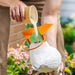 Person pouring rice into a white container with an orange funnel against a blurred garden background