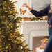 Person decorating a Christmas tree with a butterfly ornament in a festive living room.