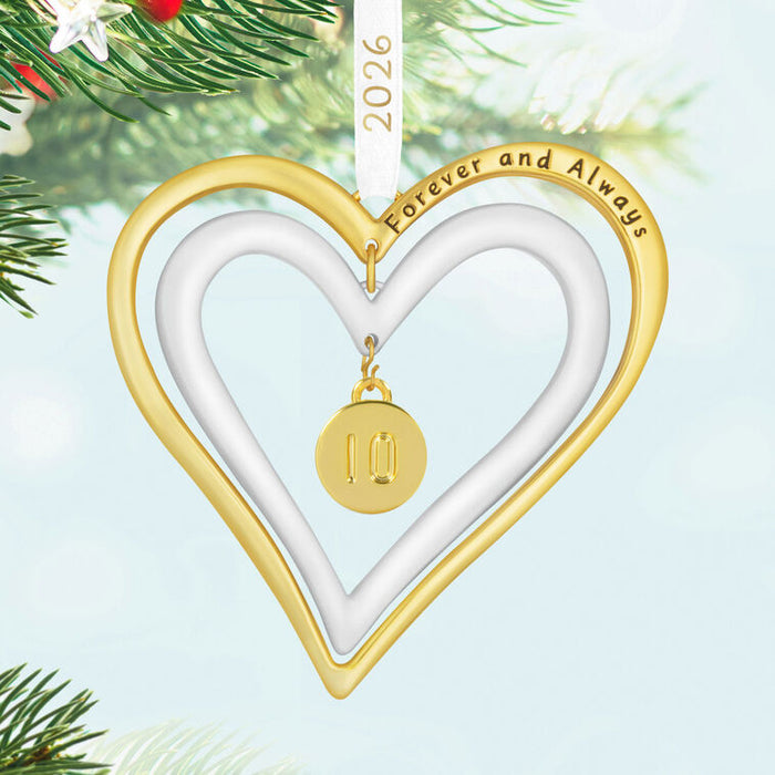 Heart-shaped ornament with 'Forever and Always' text and a gold pendant, hanging on a Christmas tree.