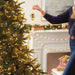 Person decorating a Christmas tree with an ornament in a festive living room.
