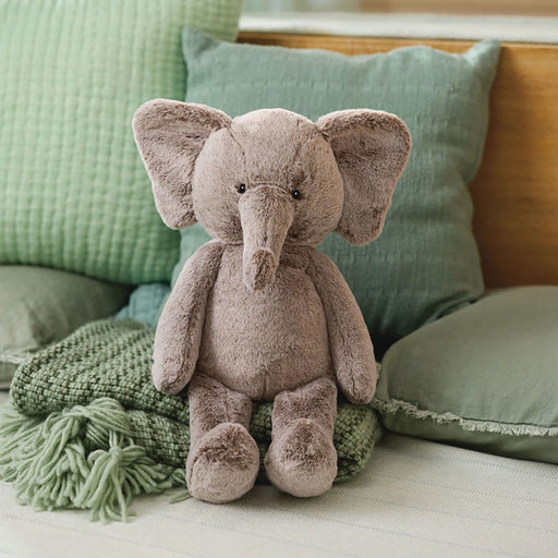 Plush elephant toy on a soft surface with green pillows and a blanket in the background