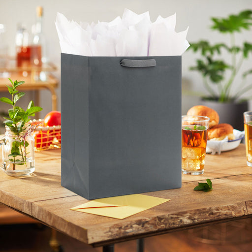 Gray gift bag with white tissue paper on a wooden table with drinks and snacks.