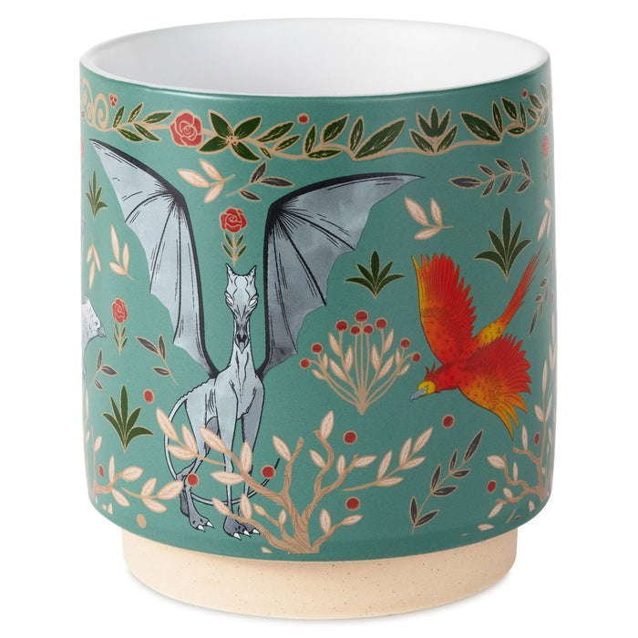 A cylindrical ceramic planter with a white interior and a speckled beige base, decorated with a teal background and an illustration of a gray bat, a red and yellow bird, and botanical motifs.