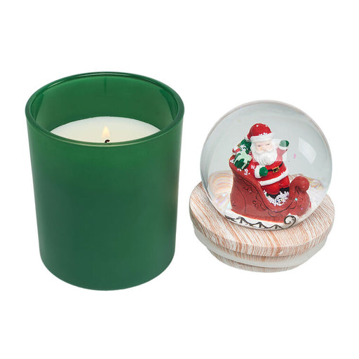 Green candle holder with a lit candle next to a Santa Claus snow globe on a white background