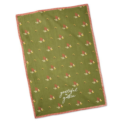 An olive green tea towel with a repeating autumn leaf pattern and a red gingham border, featuring the white script text 'grateful to gather' near the bottom.