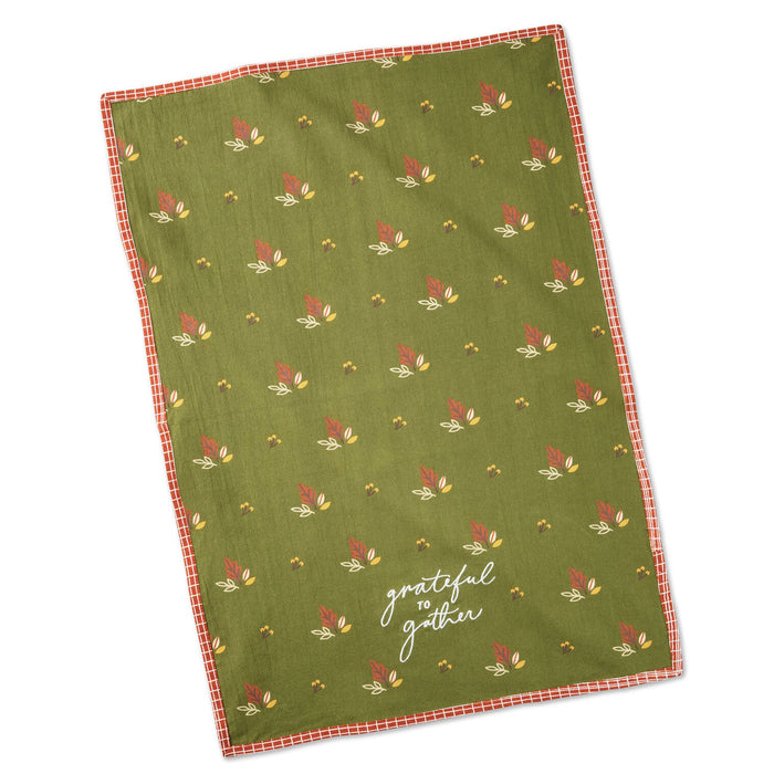 An olive green tea towel with a repeating autumn leaf pattern and a red gingham border, featuring the white script text 'grateful to gather' near the bottom.