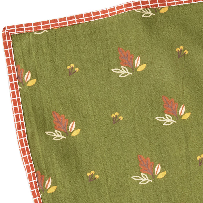 An olive green fabric item, likely a quilt or blanket, featuring a repeating pattern of small red, yellow, and white leaves. It has a red and white checkered border visible along the top and left edges.
