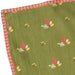 An olive green fabric item, likely a quilt or blanket, featuring a repeating pattern of small red, yellow, and white leaves. It has a red and white checkered border visible along the top and left edges.