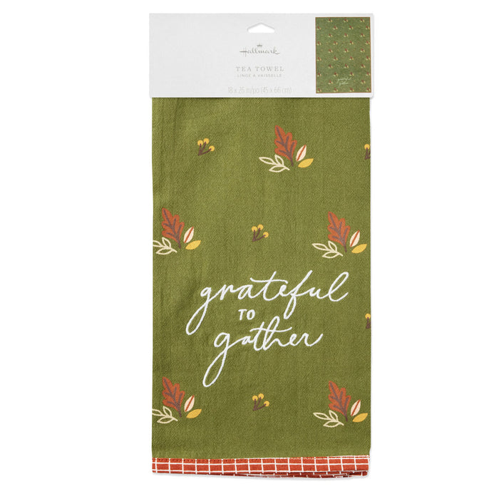 An olive green tea towel with a 'grateful to gather' script print and autumn leaf motifs, packaged on a white cardboard header with the Hallmark brand visible.
