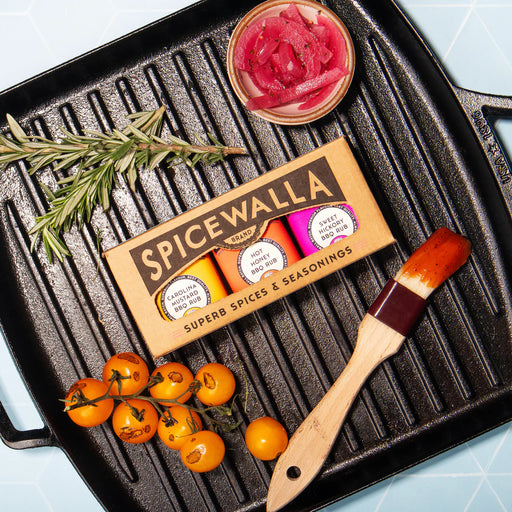 SpiceWalla seasoning packet on a grill with tomatoes, rosemary, and a brush.
