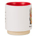 A white ceramic mug with a vibrant red interior and a natural beige clay foot ring. The side of the mug features black text and a colorful graphic illustration.