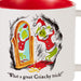 A white ceramic mug with a red interior, featuring a Grinch-themed illustration of the Grinch looking at his mirror in a Santa suit and the text 'What a great Grinchy trick!'.