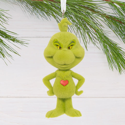 Green character with a red heart hanging from a Christmas tree.
