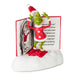 A collectible figurine of the Grinch standing on a white base with an open book behind him, wearing a red Santa hat and coat with white trim and red slippers.