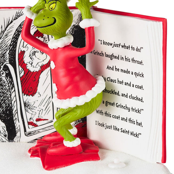 A Grinch figurine in a red Santa-style dress with white trim, posed in front of an open Dr. Seuss book.