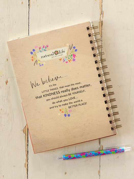 Notebook with a message about kindness on a wooden surface, accompanied by a colorful pen.