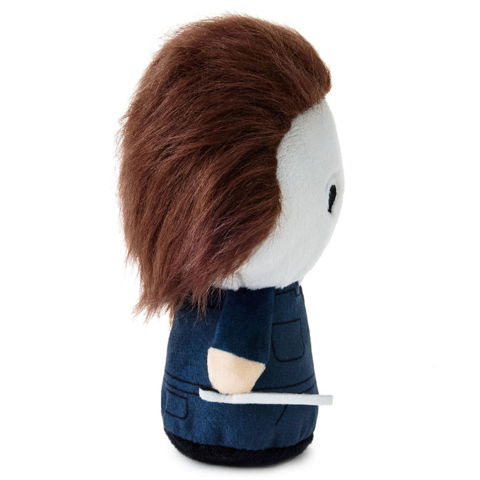 A small plush doll with brown hair, a white face, a dark blue outfit, and a beige arm detail, shown against a plain white background.