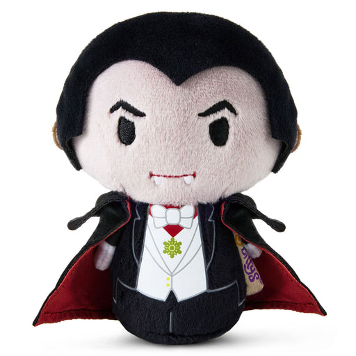 A plush vampire doll with black hair, a pale face, a black tuxedo, white shirt, red cape lining, and small vampire fangs, photographed on a plain white background.